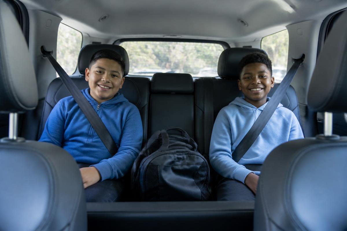 Two students riding in the back seat of a clean vehicle with seatbelts fastened